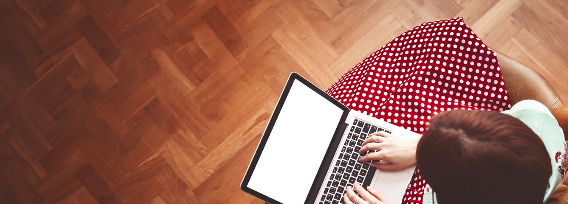 Een vrouw met een rode rok met witte stippen zit in een bruine stoel achter haar laptop