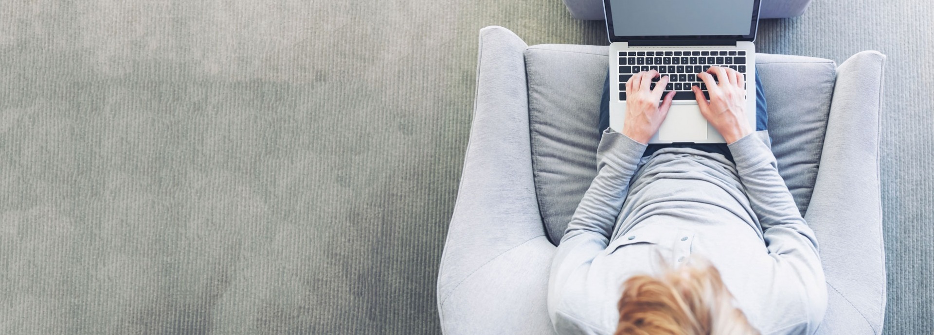 Een vrouw zit in een grijze stoel achter haar laptop 