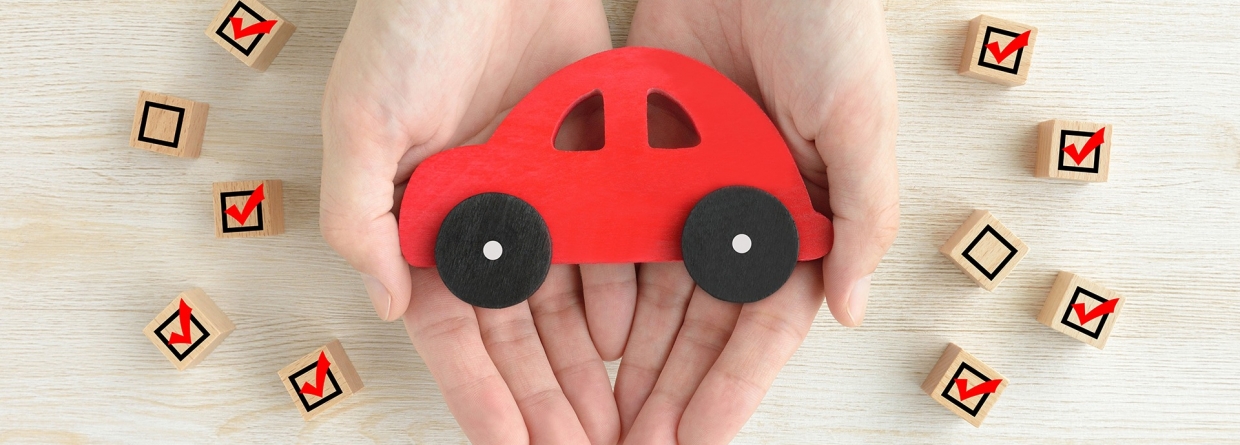 Houten speelgoed auto in handen van een mens en omringd met blokjes waarop wel en geen vinkjes staan