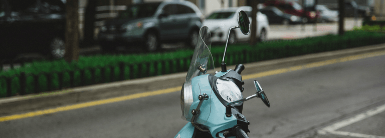 Een blauwe scooter met op de achtergrond de weg
