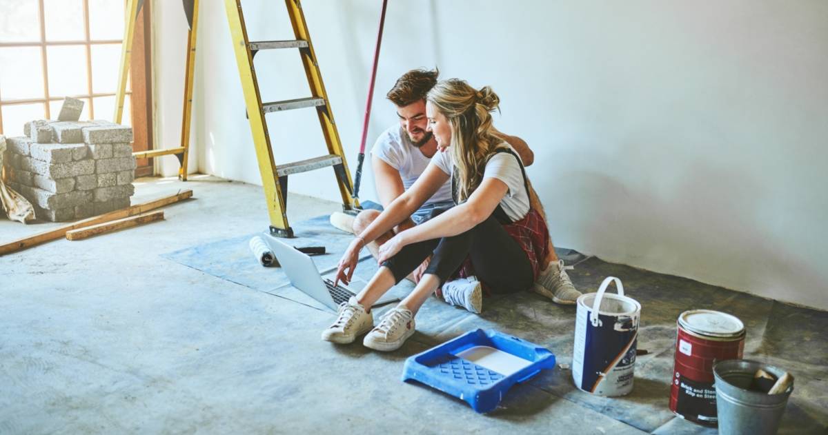 Jong stel zittend in nieuw huis met trap en verfpotten om zich heen