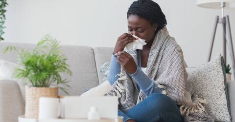 Donkere vrouw heeft last van verkoudheid en de griep en ze controleert haar temperatuur