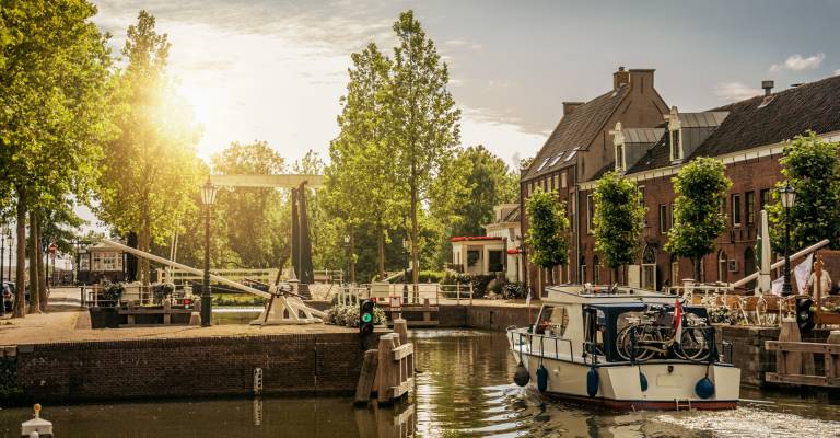 Boot langs een met bomen omzoomde smalle gracht in de zonsopgang bij Weesp. Rustig en gezellig dorp vol grachten en groen vlakbij Amsterdam.