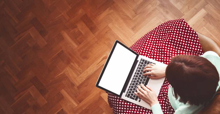 Een vrouw met een rode rok met witte stippen zit in een bruine stoel achter haar laptop